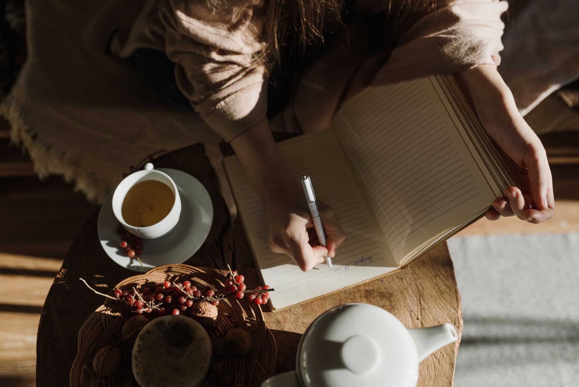 Persona escribiendo en un diario de bienestar emocional junto a una taza de té, ambiente tranquilo
